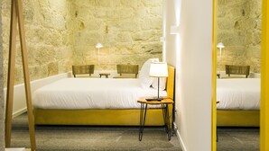 Een hotelkamer met een stenen muur, twee bedden, een tafeltje met een lamp en een houten ladder.