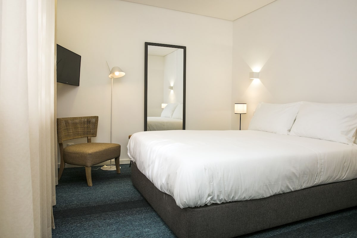 Een hotelkamer met een groot bed, een stoel, een flatscreen-tv en een spiegel.