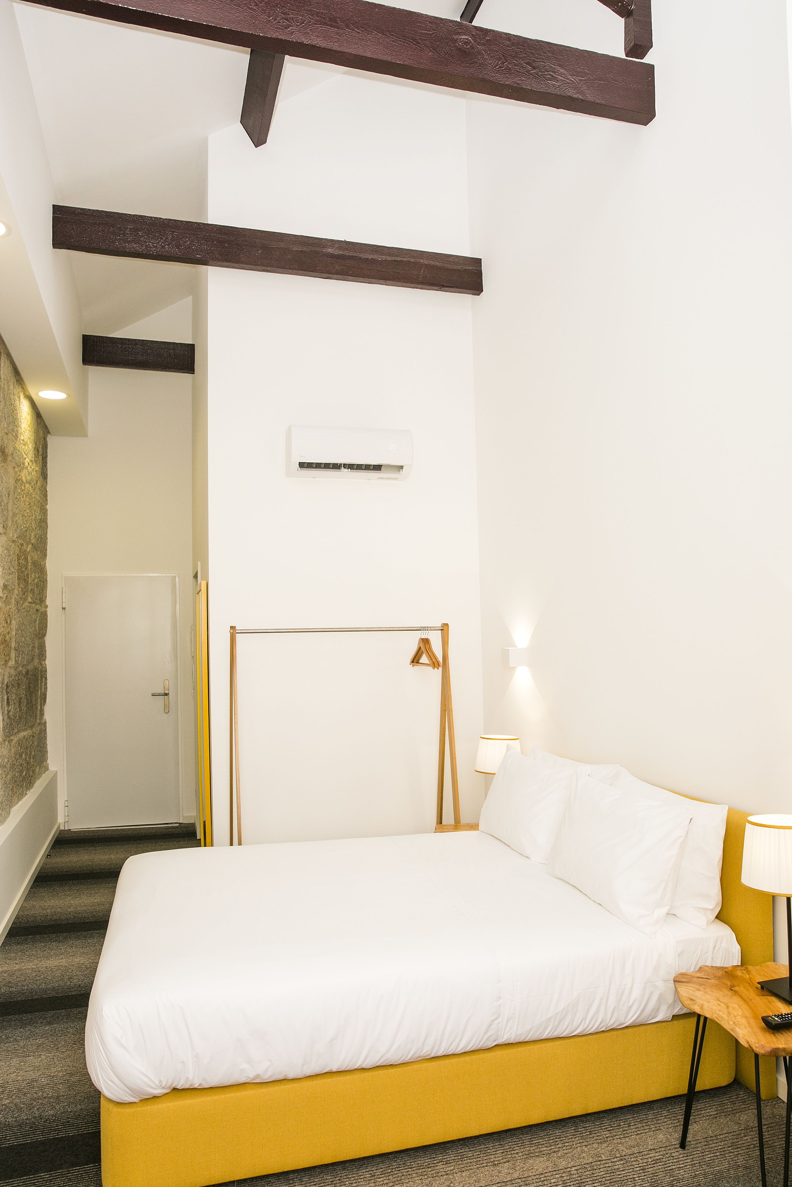 A hotel room with a bed, a bedside table with a lamp, a wardrobe, and a door.