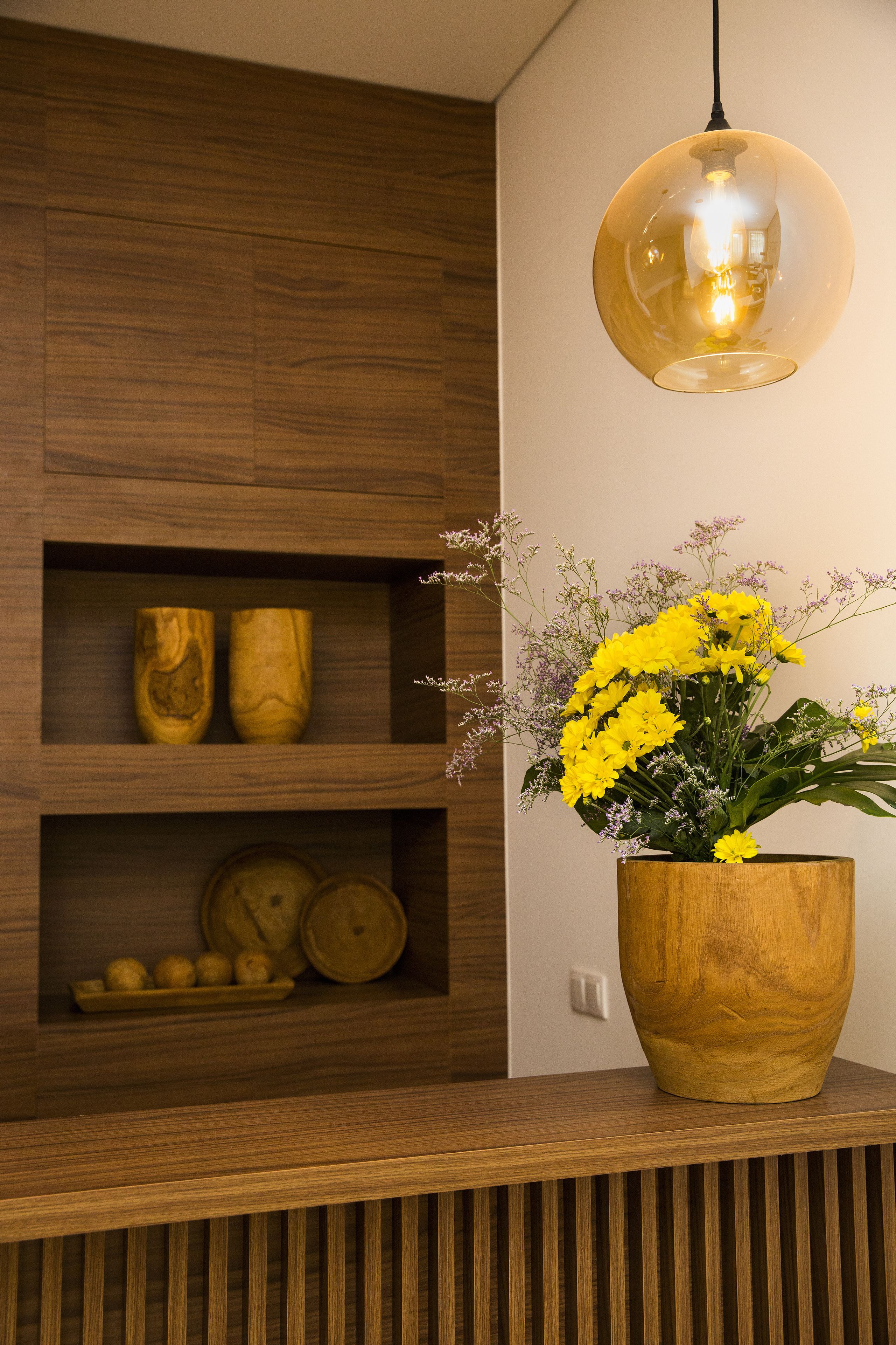 A wooden shelf with decorative items and a vase of yellow flowers.
