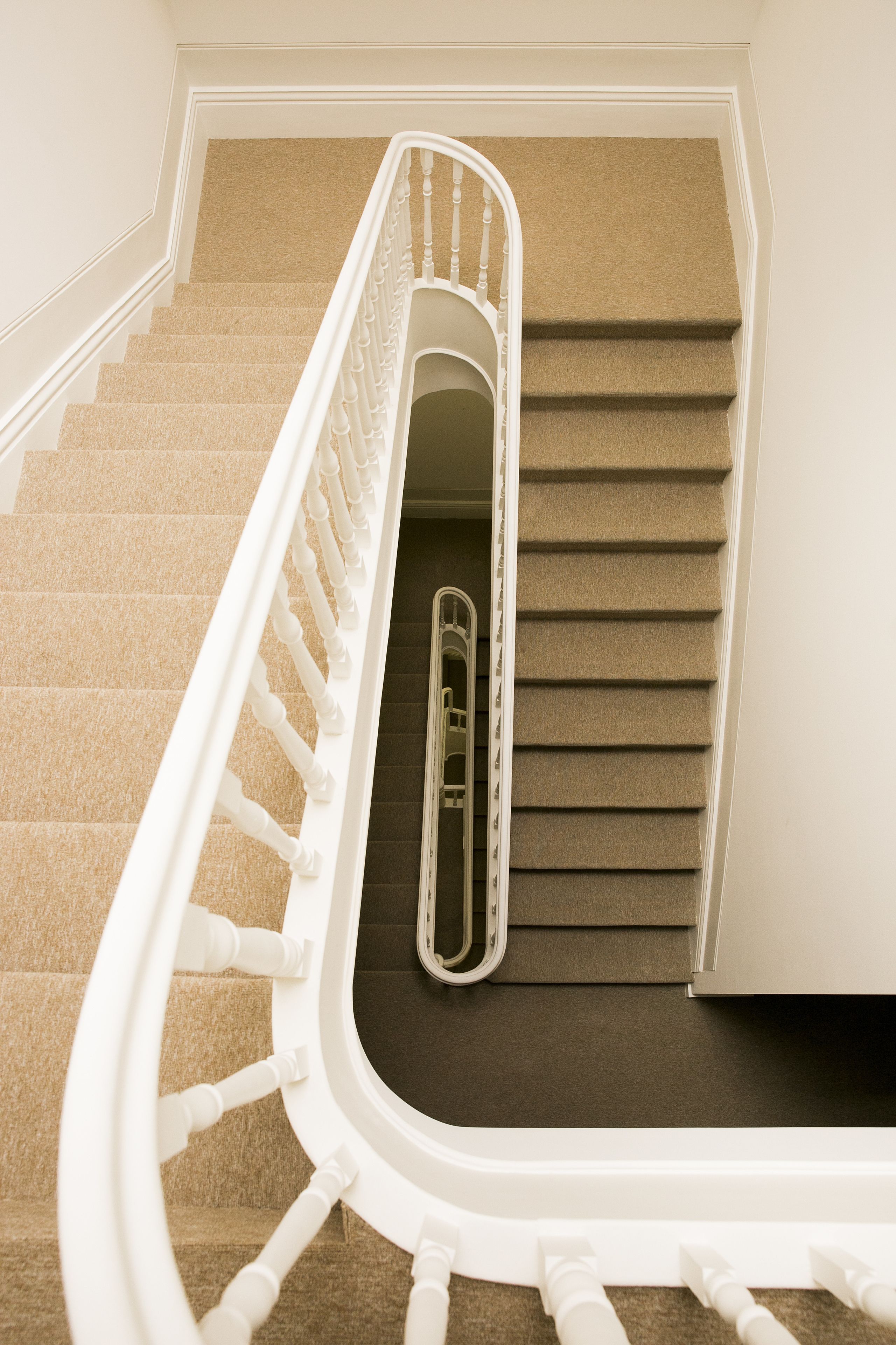A carpeted staircase with white balusters and a handrail, leading to a landing with a door.