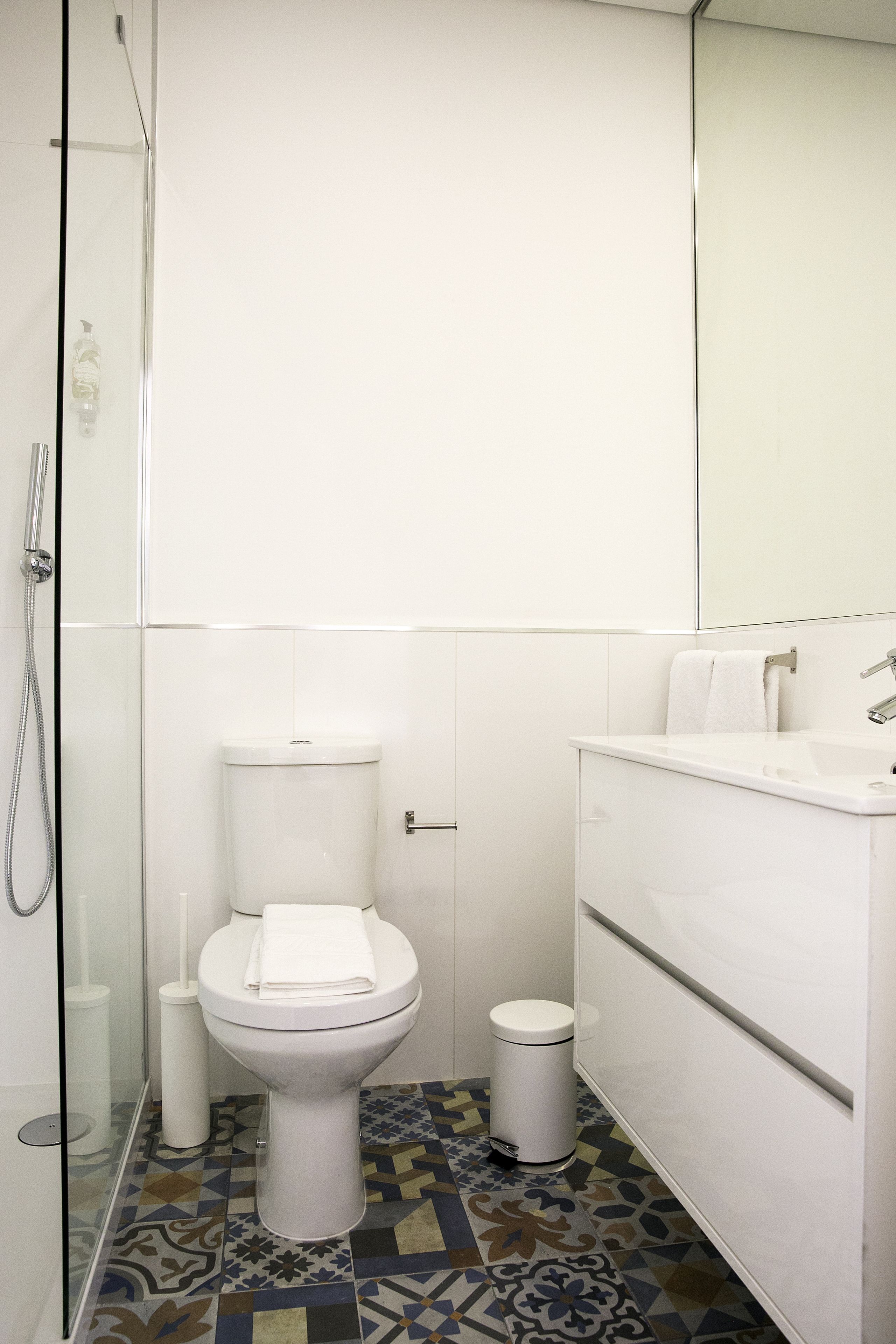 A bathroom with a toilet, a sink, a mirror, and a shower.