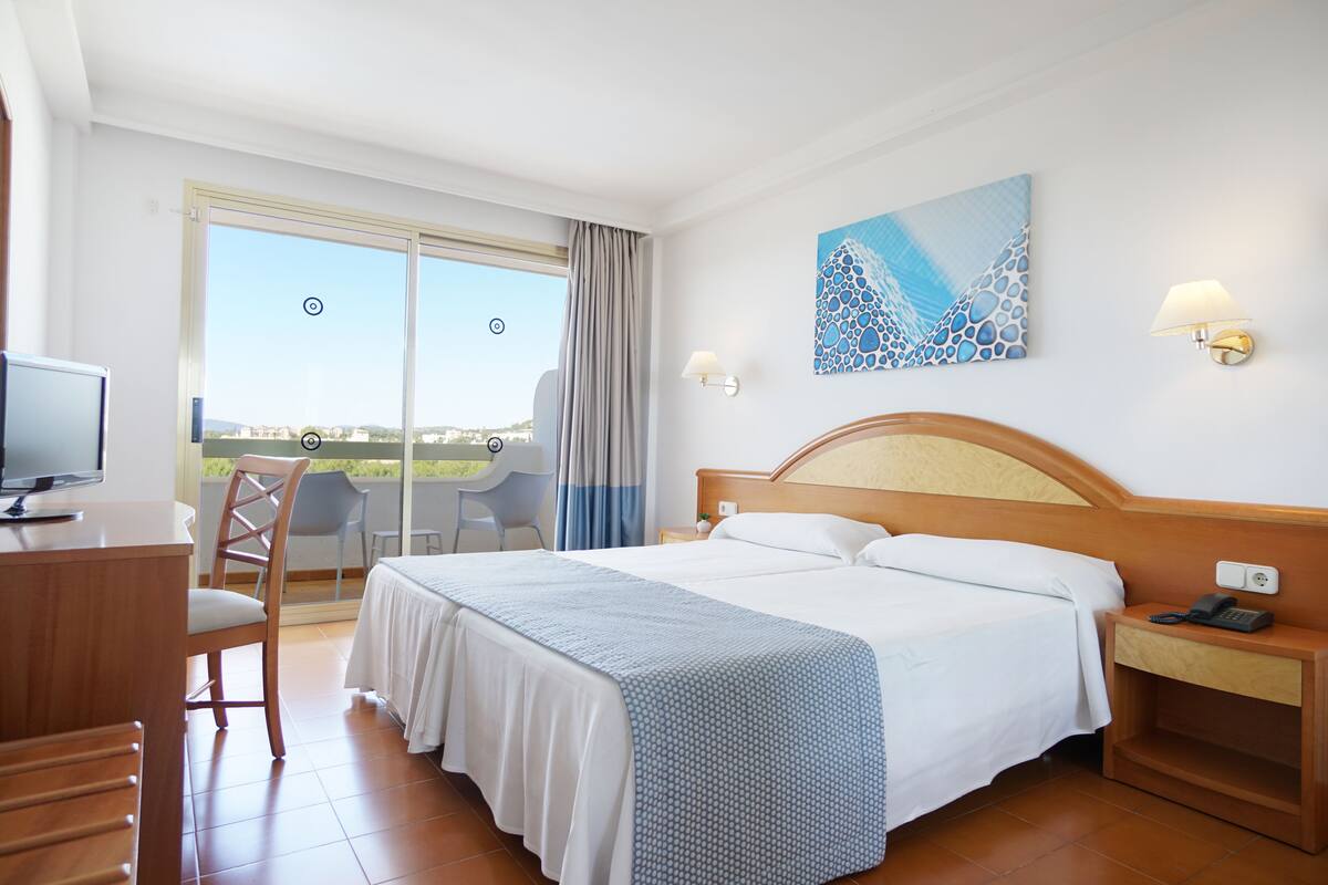 A hotel room with a bed, a desk, a chair, a TV, and a view of the outdoors.