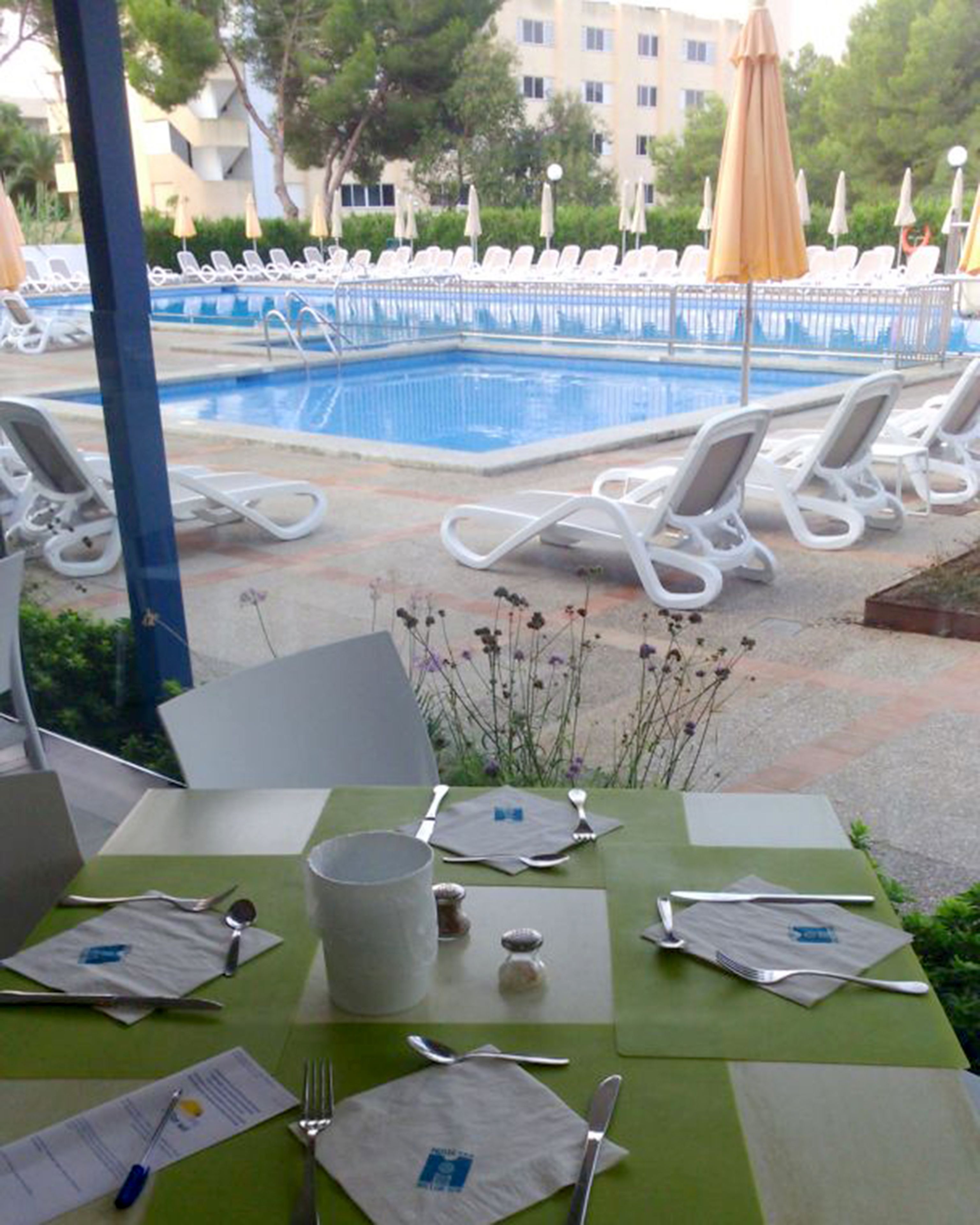 A dining area with a pool view, including a table set with cutlery and a menu, and white lounge chairs around the pool.