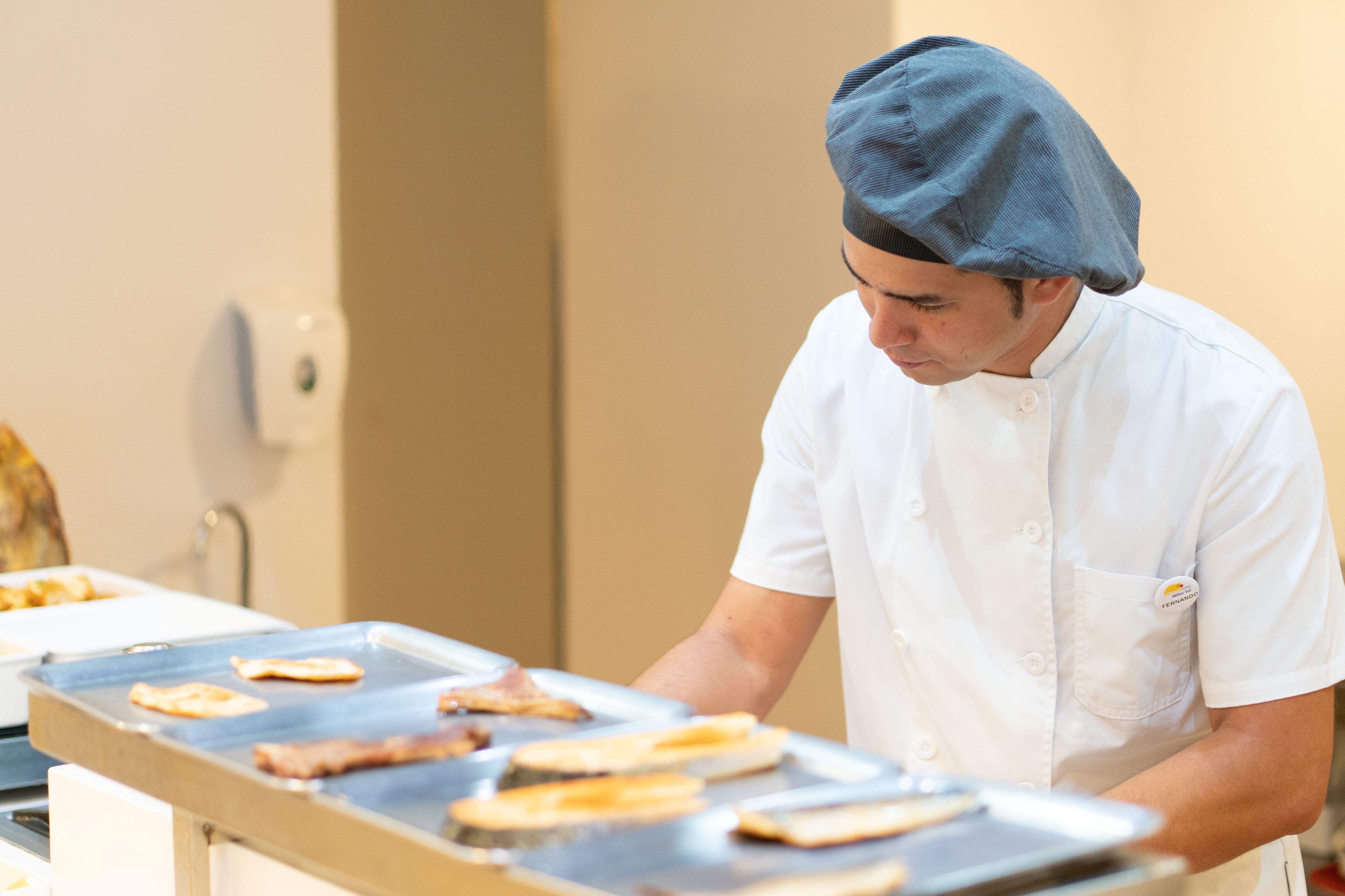 A chef preparing food in a kitchen with a stainless steel countertop and a white wall in the background.