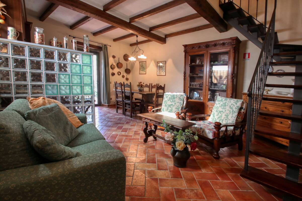 A cozy living room with a green sofa, wooden chairs, a dining table, and a staircase.