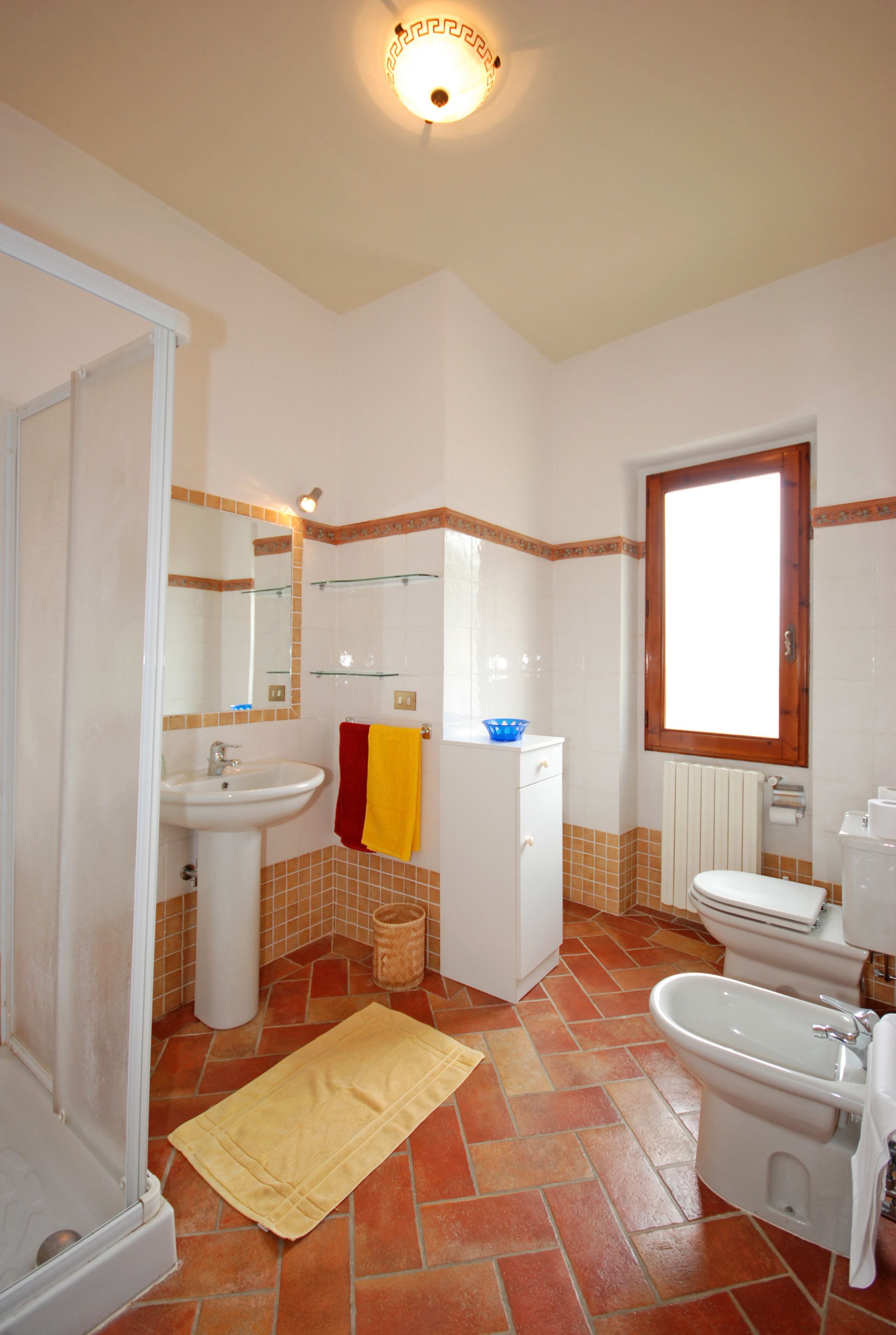 A bathroom with a sink, toilet, and bidet, tiled floor, and a window.