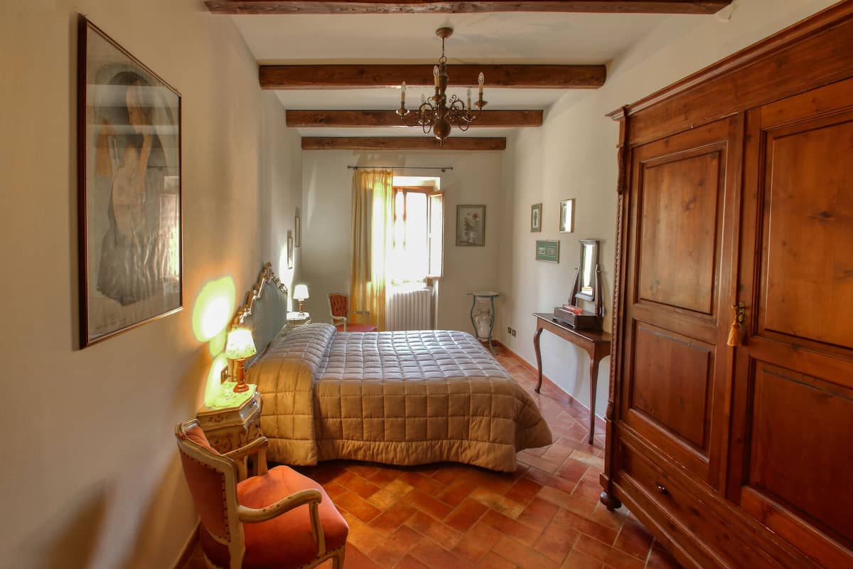 A bedroom with a large bed, wooden wardrobe, and a chair.