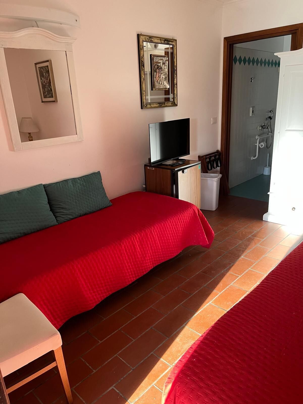 A bedroom with a red bed, a television, a small cabinet, and a bathroom visible through an open door.