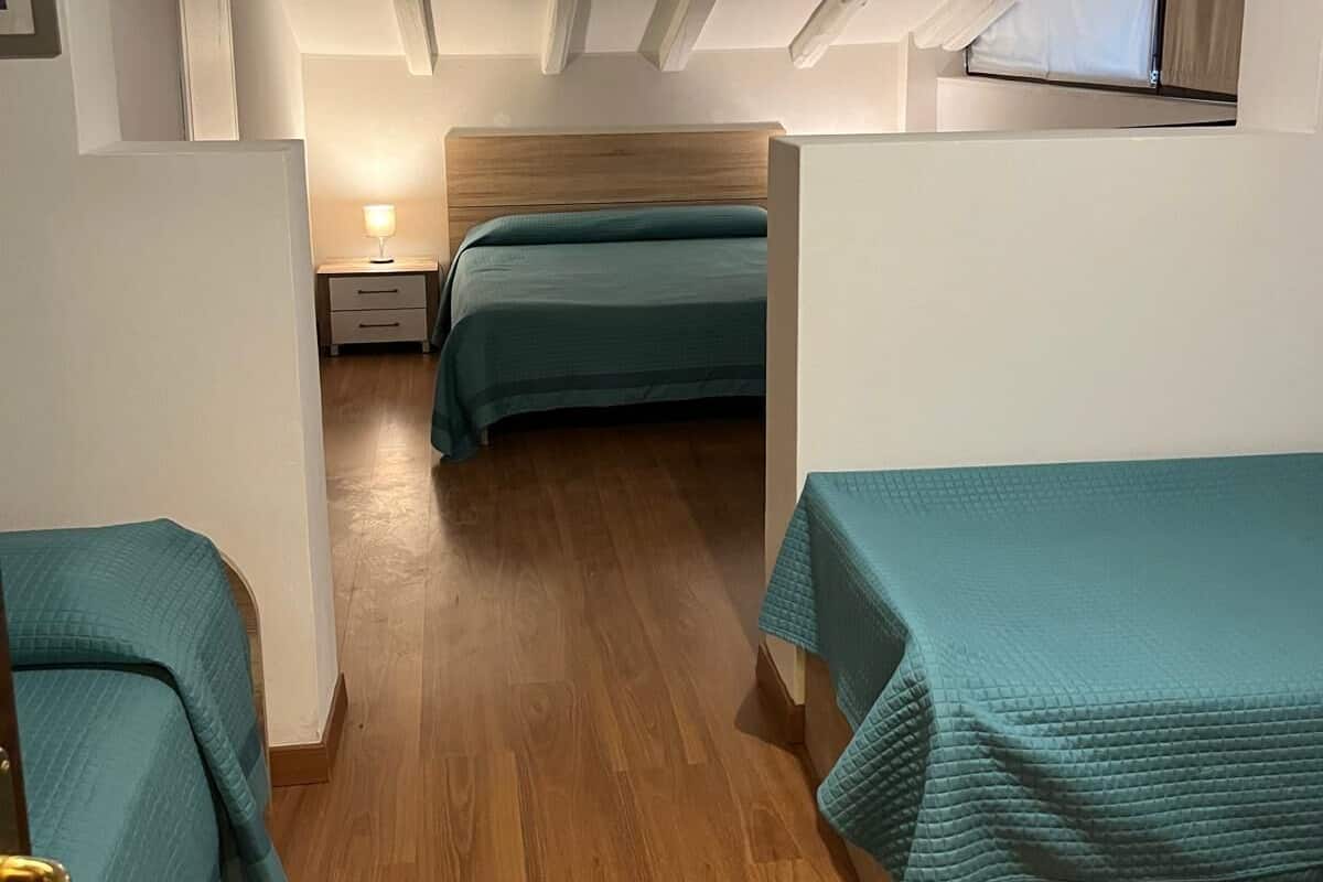 Un couloir étroit mène à une chambre dotée d’une tête de lit en bois, d’une table de chevet et d’une fenêtre.