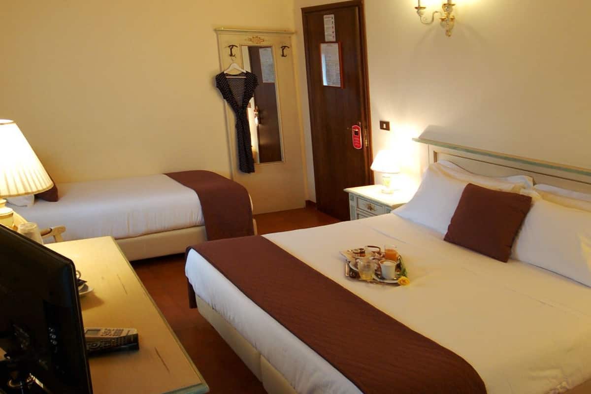 Une chambre d’hôtel avec deux lits simples, un bureau avec un ordinateur, une lampe et un climatiseur fixé au mur.