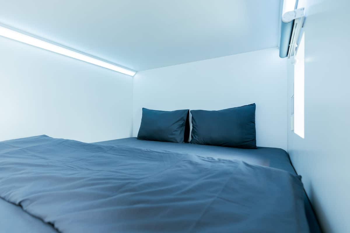 A small, modern room with a single bed, a ceiling light, and a window.