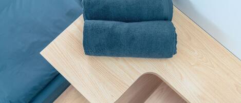A neatly folded dark blue towel on a wooden side table.