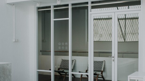 A modern room with a glass door leading to a balcony, a white table, and two patterned chairs. - Bobopod Paskal, Bandung (Bandung)