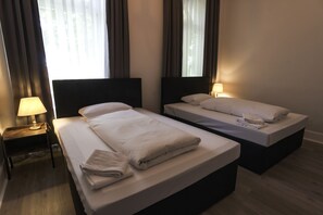 Una habitación de hotel con dos camas, una mesita de noche con lámpara y una ventana con cortinas.