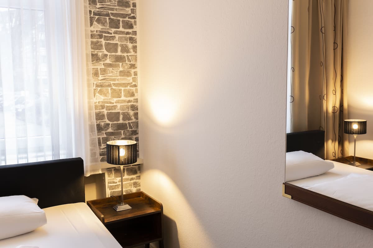 A hotel room with a stone wall, a bed with white linens, a bedside table with a lamp, and a mirror above the bed.