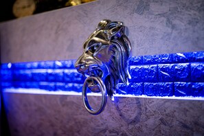 Escultura de cabeza de león metálico montada en una pared con un panel azul iluminado.