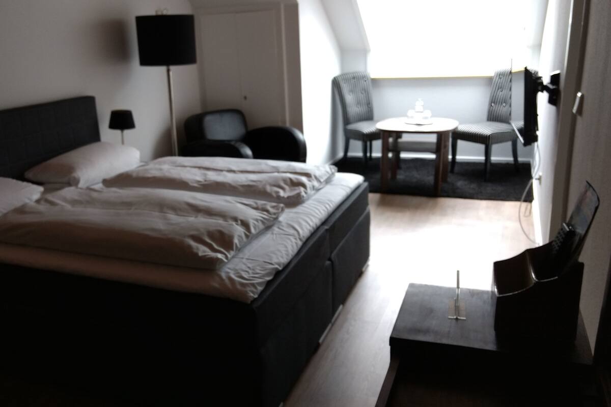 A hotel room with a bed, a desk, a chair, and a small table.