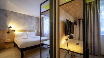 Una habitación de hotel moderna con cama, lámpara de noche y televisión montada en la pared.