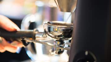 A close-up of a coffee machine with a metal cup and a hand holding a spoon.