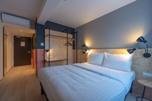 Una camera d'albergo moderna con un letto grande, un armadio in legno e una scrivania con una sedia.