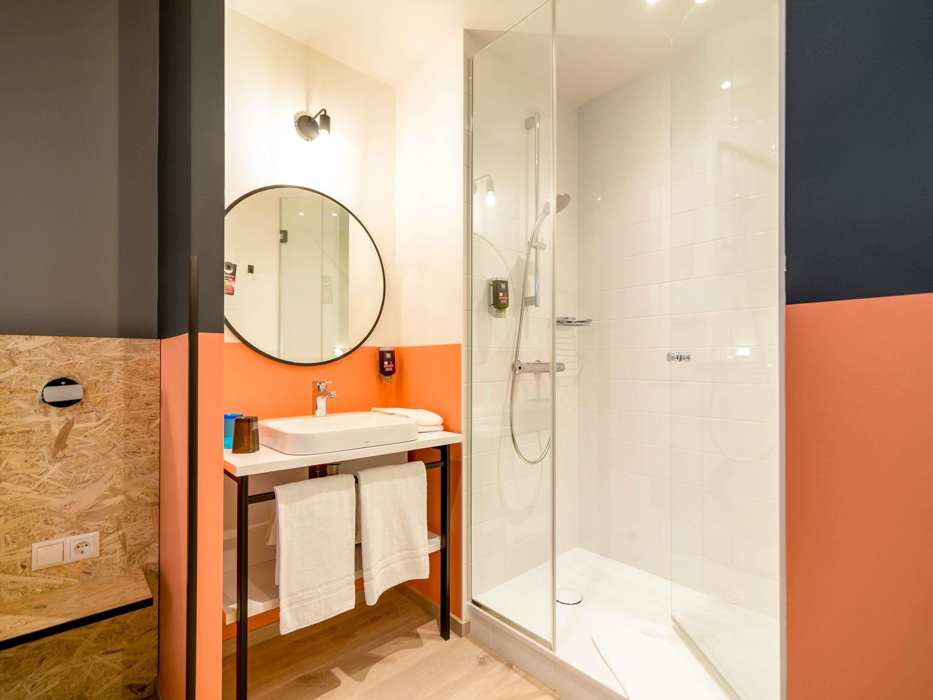 A modern bathroom with a glass-enclosed shower, a round mirror, and a sink with a towel rack.