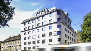 Un edificio de varios pisos con un estilo arquitectónico moderno, que destaca por su diseño en esquina y numerosos ventanales.