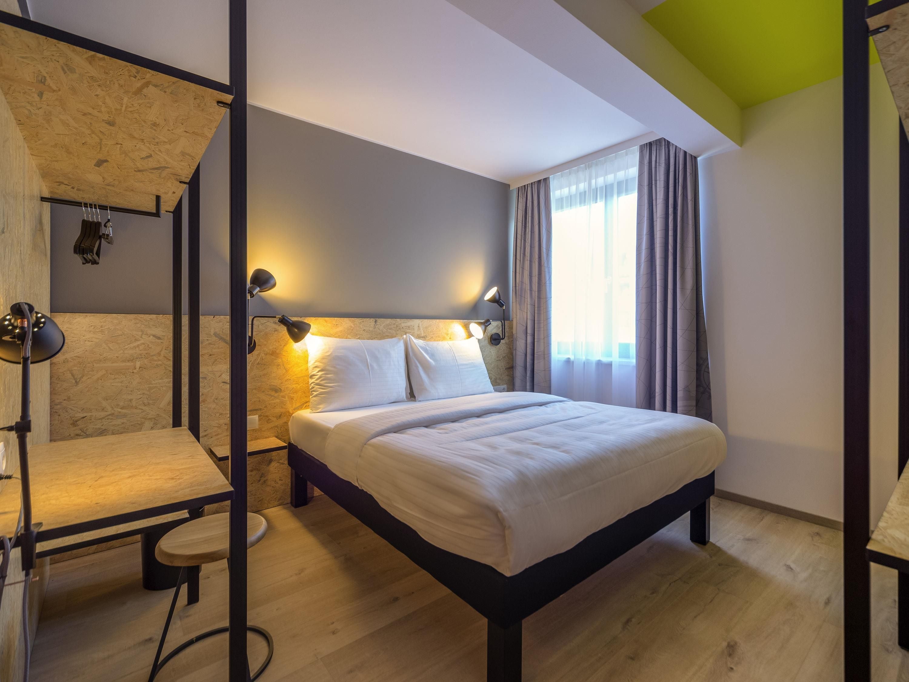 A modern bedroom with a wooden headboard, a bed with white linens, and a desk with a chair.