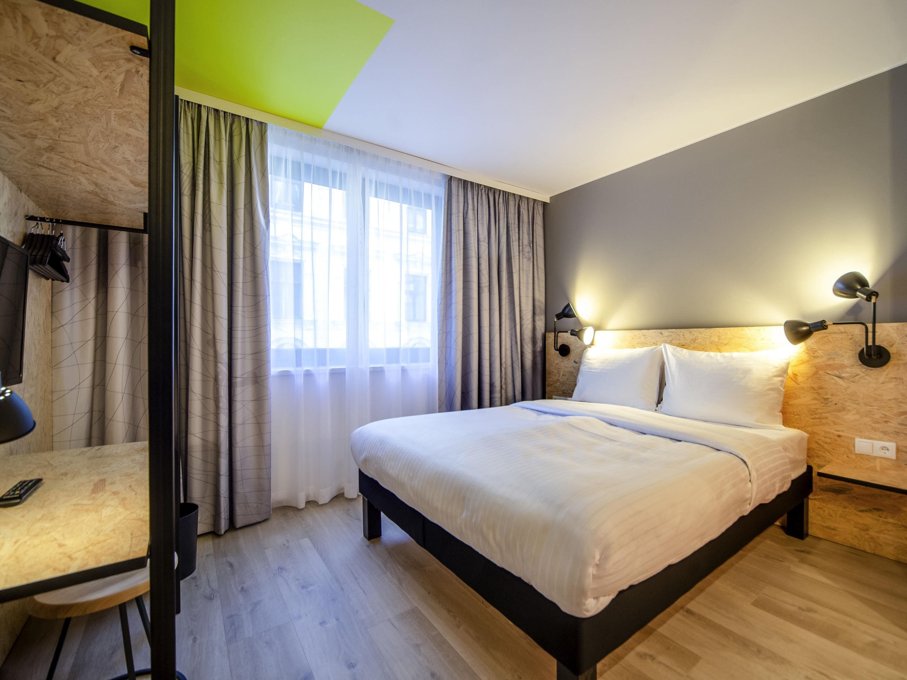 Hotelkamer met een bed, een bureau, een stoel, een raam met gordijnen en een wandlamp.