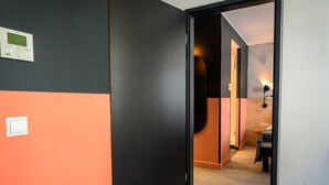 A hallway with a black and orange wall, a door leading to a room with a wooden floor, and a wall-mounted light fixture. - ibis Styles Wien Messe Prater (Vienna)