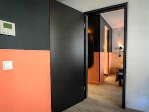 A hallway with a black and orange wall, a door leading to a room with a wooden floor, and a wall-mounted light fixture. - ibis Styles Wien Messe Prater (Vienna)