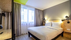 Habitación de hotel con cama, escritorio, lámpara y ventana con cortinas.