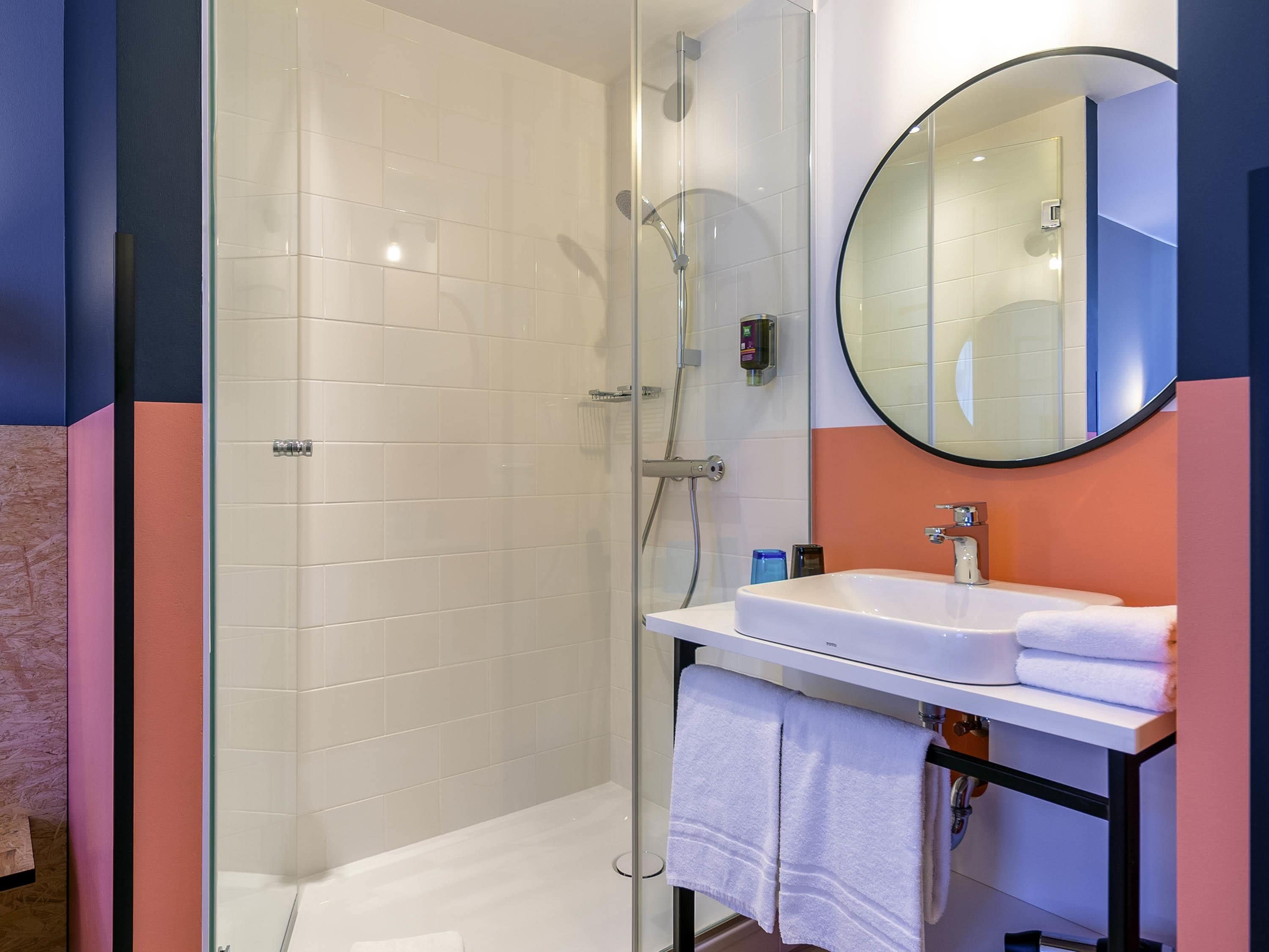 A bathroom with a glass-enclosed shower, a white sink, and a round mirror.