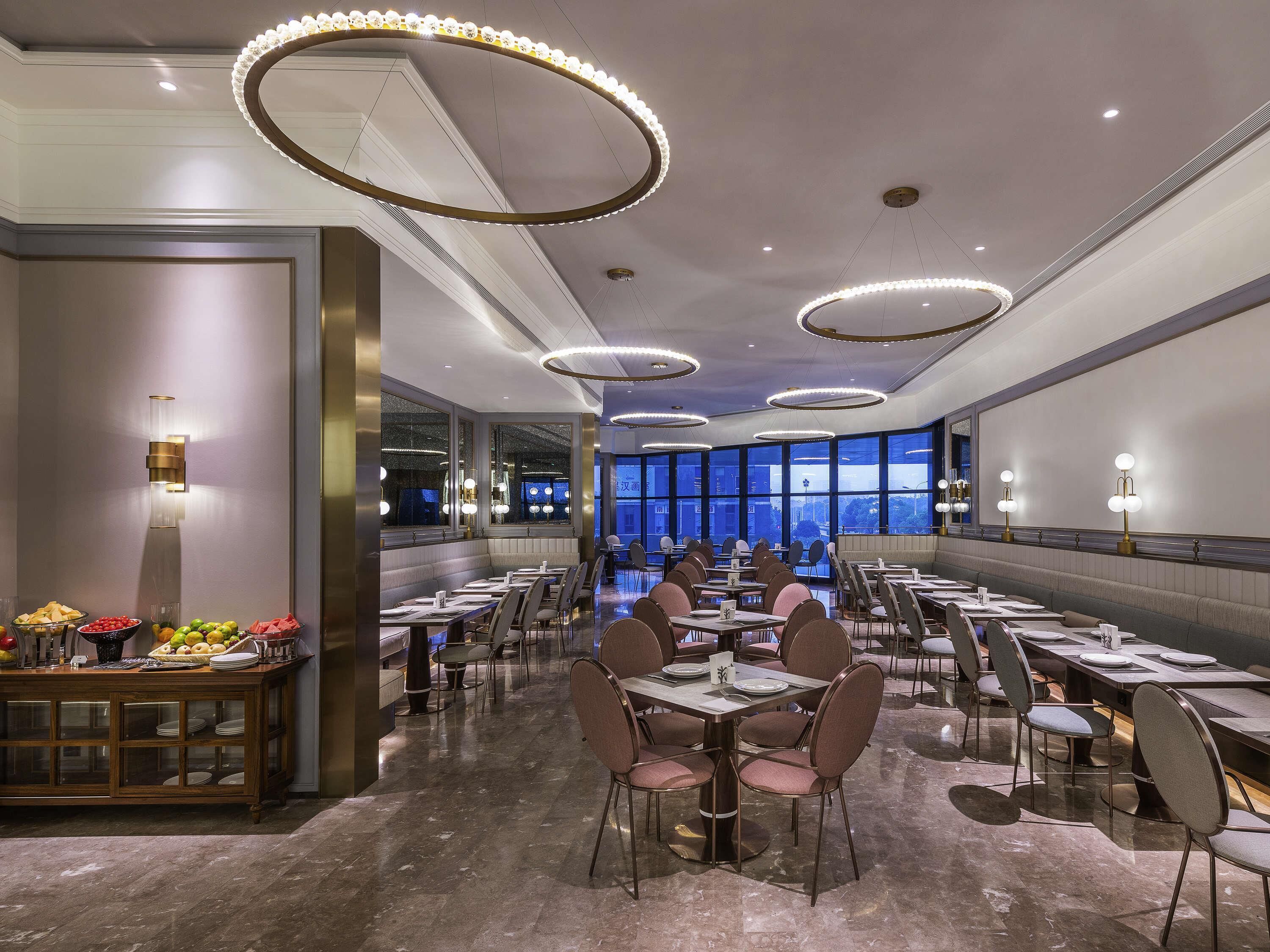 A spacious dining area with multiple tables and chairs, large windows, and modern lighting fixtures.