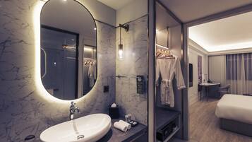 A modern hotel bathroom with a large oval sink, a mirror, and a shower area.