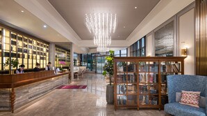 A spacious lobby with a reception desk, a large chandelier, a seating area with a blue sofa, and a bookshelf. - Mercure Suzhou Jinji Lake (Suzhou)