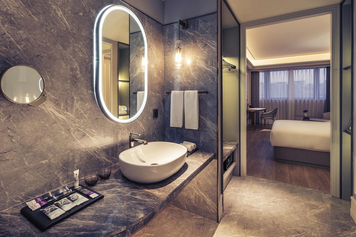 A modern bathroom with a large oval mirror, a sink, and a vanity with toiletries.