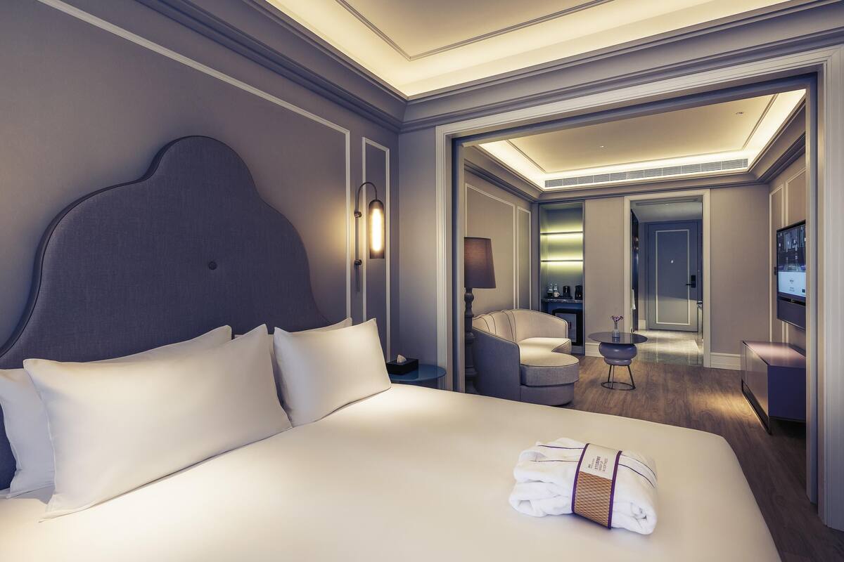 Een moderne hotelkamer met een groot bed, een nachtkastje, een lamp, een zithoek met een stoel en een klein tafeltje, en een televisie.