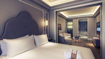 A modern hotel room with a large bed, a nightstand, a lamp, a seating area, and a television.