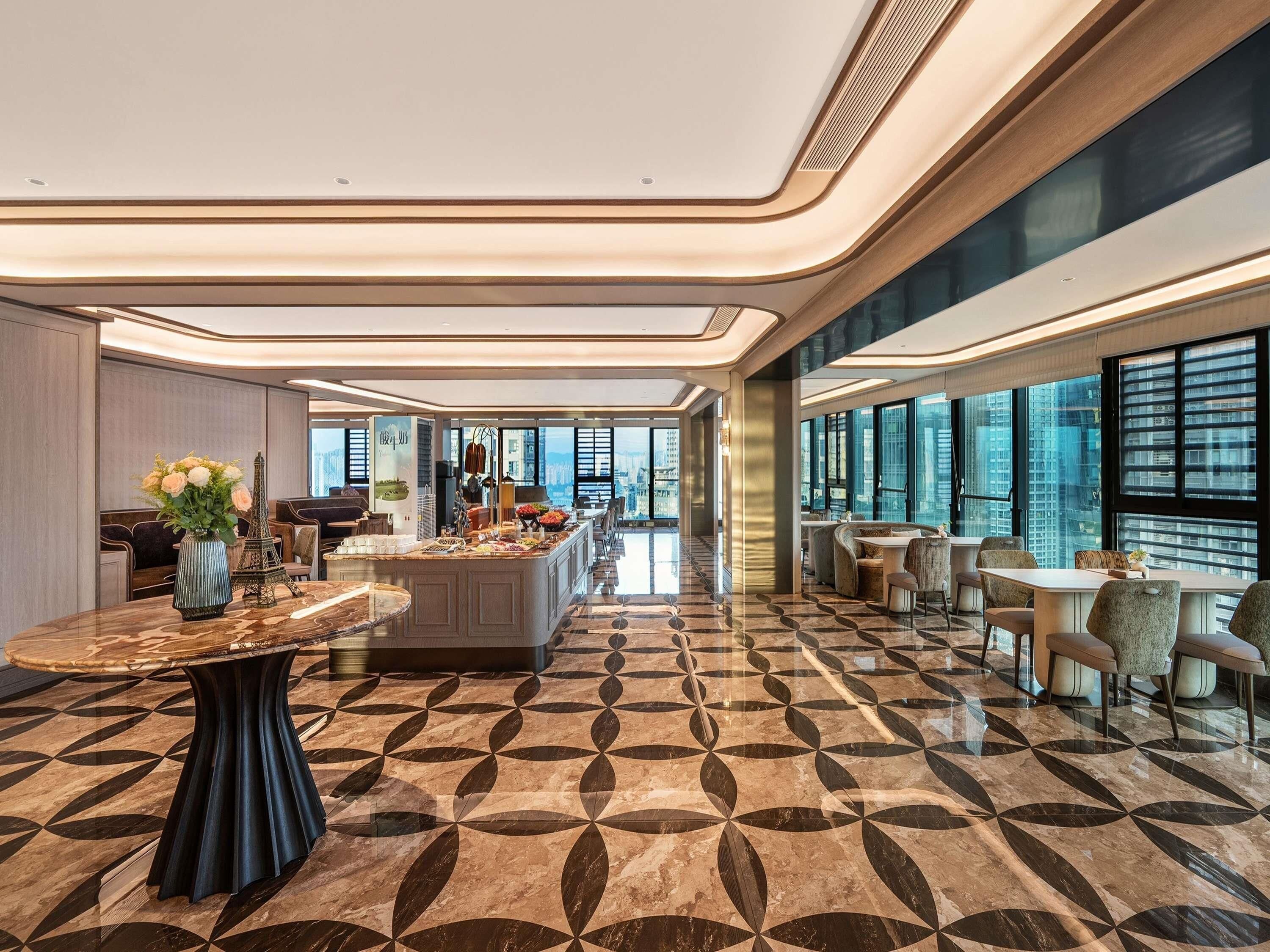 Een ruime hotellobby met een centraal eiland, zitgedeeltes en grote ramen met uitzicht over de stad.