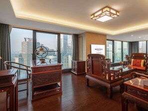Une chambre d’hôtel spacieuse dotée d’une grande fenêtre donnant sur la ville, d’un bureau en bois traditionnel, d’un canapé confortable et d’un luminaire moderne au plafond.
