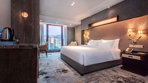 Habitación de hotel con una cama grande, un escritorio con hervidor, una silla y vistas a la ciudad.