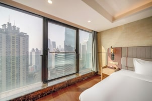 Una habitación de hotel moderna con un ventanal grande, una cama, una mesita de noche y una lámpara de pared.