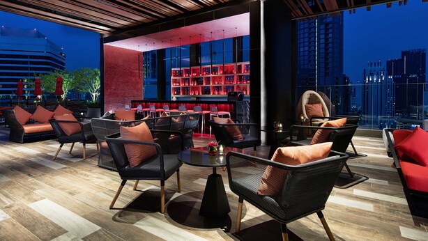 Un área de estar moderna con asientos y bar, con vista a la ciudad.