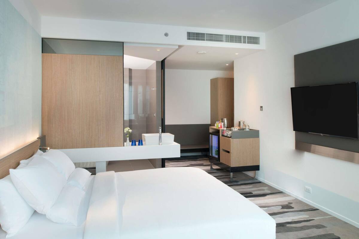 Een moderne hotelkamer met een groot bed, een ingebouwd bureau, een flatscreen televisie, een spiegel en een kleine kitchenette.