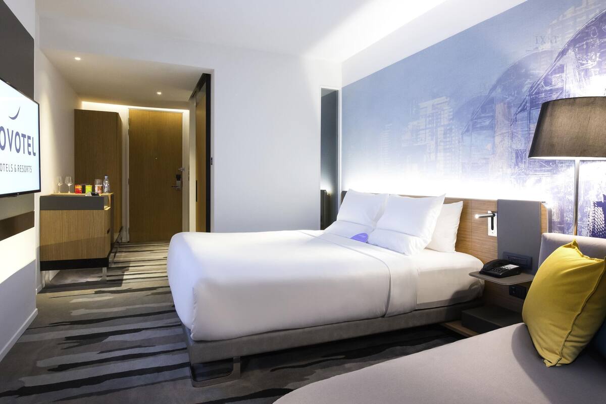 Een hotelkamer met een bed, nachtkastje, lamp en uitzicht op een stadsbeeld.