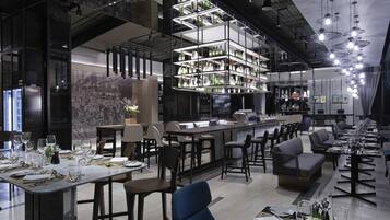 A modern restaurant interior with high ceilings, exposed ductwork, and a bar area with shelves of bottles.