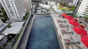 Una piscina en la azotea con sillones de descanso y sombrillas, rodeada de edificios altos.