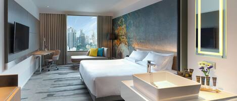 A hotel room with a bed, a desk, a TV, a large window, and a bathroom with a sink and mirror.