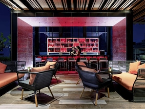 Un espace bar doté de sièges et d’un comptoir, avec un design moderne, un éclairage rouge et une variété de bouteilles.